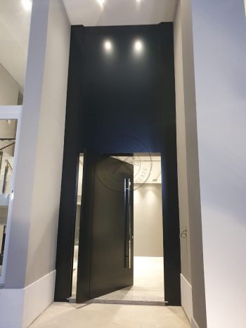 Porta pivotante em ACM preto carbono com um friso vertical e um friso horizontal, bandeira superior e dupla vedação - Imagem 3