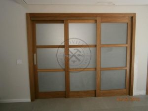 Porta com sistema de correr embutido com três folhas sobrepostas, vidro jateado 8 mm, pintura de verniz P.U acetinado (Sayerlack)