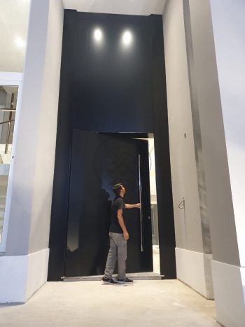 Porta pivotante em ACM preto carbono com um friso vertical e um friso horizontal, bandeira superior e dupla vedação - Imagem 6