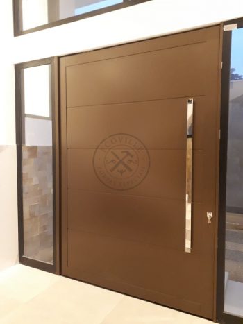 Porta pivotante em ACM bronze com borda e frisos horizontais, painéis de vidro panorâmico e dupla vedação