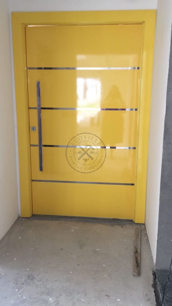 Porta pivotante com revestimento em MDF, frisos em inox e pintura laca P.U amarelo brilhante