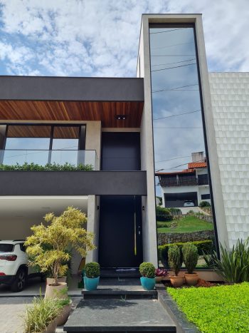 Porta pivotante em ACM preto carbono com borda e frisos horizontais e dupla vedação