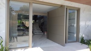 Porta pivotante em ACM Silver Gold com frisos horizontais, puxador cava, portal duplo lateral com vidro 10 mm incolor e dupla vedação - Imagem 9