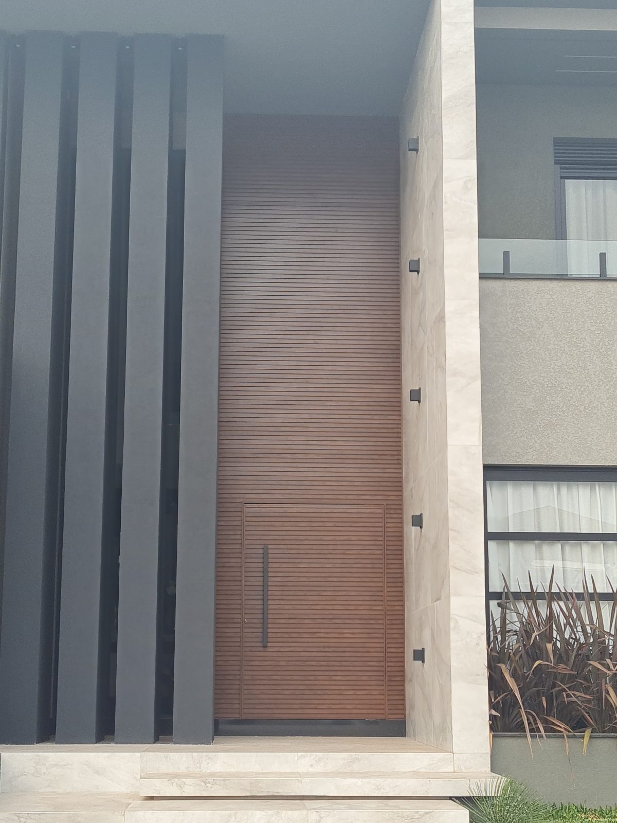 Porta pivotante em ACM amadeirado ripado na horizontal com bandeira superior e dupla vedação - Imagem 3