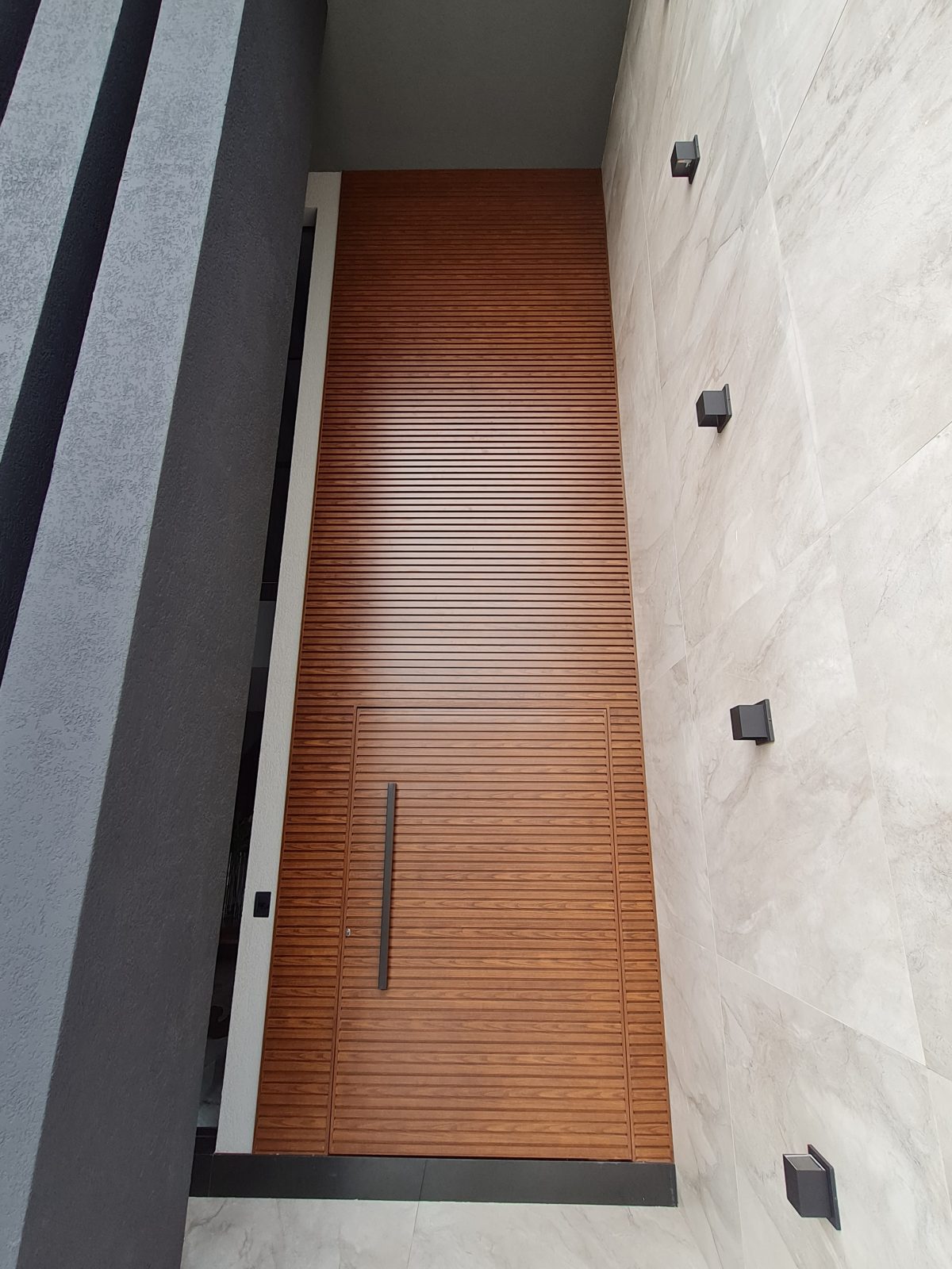 Porta pivotante em ACM amadeirado ripado na horizontal com bandeira superior e dupla vedação - Imagem 2