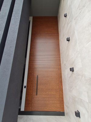 Porta pivotante em ACM amadeirado ripado na horizontal com bandeira superior e dupla vedação - Imagem 2