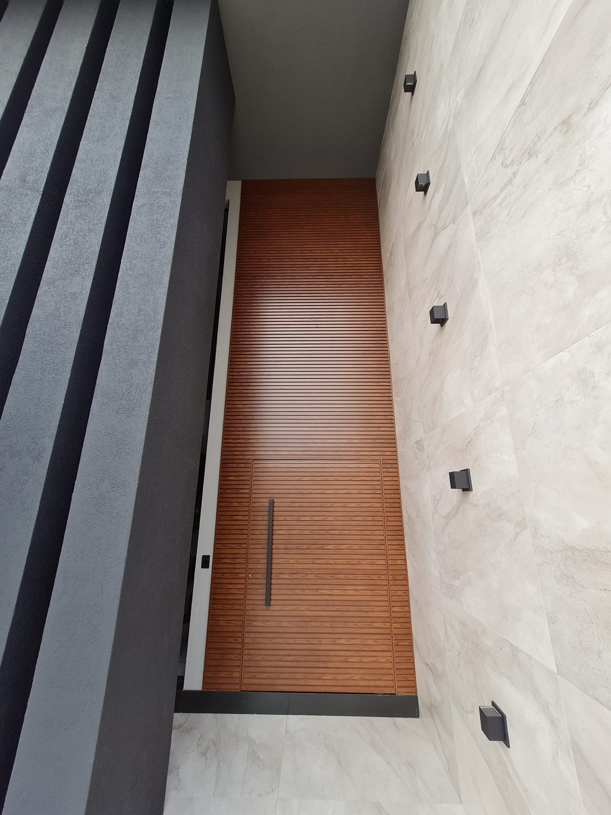 Porta pivotante em ACM amadeirado ripado na horizontal com bandeira superior e dupla vedação - Imagem 1