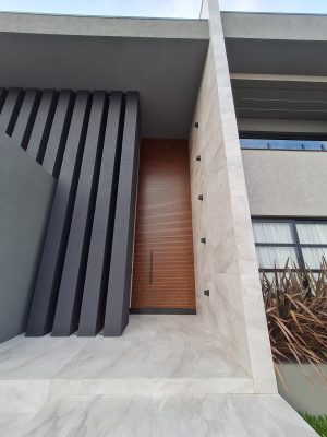 Porta pivotante em ACM amadeirado ripado na horizontal com bandeira superior e dupla vedação - Imagem 4