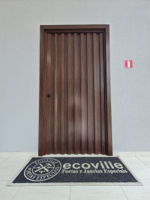 Porta pivotante em ACM Sucupira, modelo ripado na vertical com dupla vedação