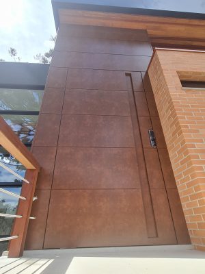 Porta pivotante em ACM aço corten com frisos horizontais, puxador cava e dupla vedação