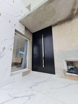 Porta pivotante em ACM preto carbono, painel lateral fixo no mesmo alinhamento da porta, puxador exposto de inox com 2 metros cromado e dupla vedação - Imagem 3