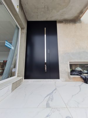 Porta pivotante em ACM preto carbono, painel lateral fixo no mesmo alinhamento da porta, puxador exposto de inox com 2 metros cromado e dupla vedação - Imagem 4