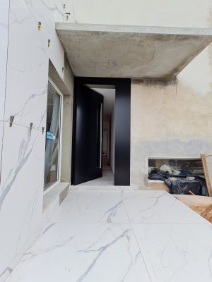 Porta pivotante em ACM preto carbono, painel lateral fixo no mesmo alinhamento da porta, puxador exposto de inox com 2 metros cromado e dupla vedação - Imagem 5