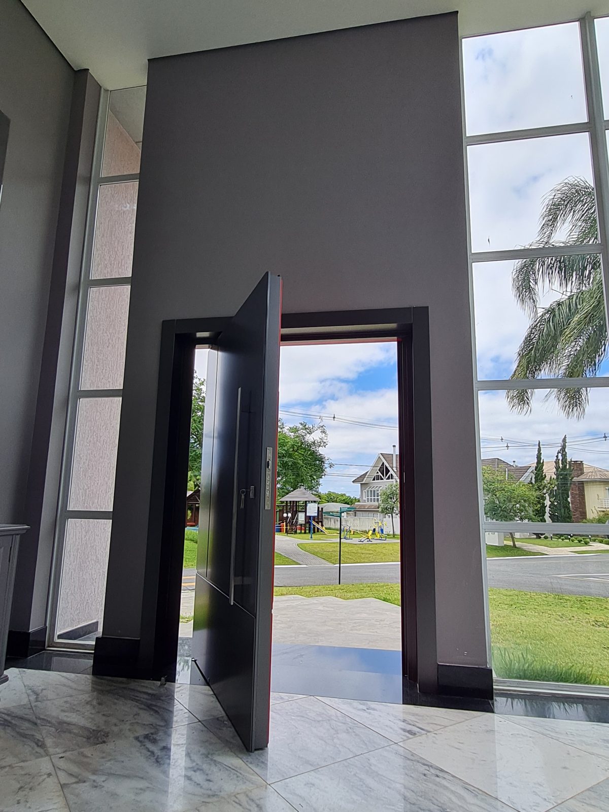 Porta pivotante em ACM com duas cores. Lado externo vermelho fosco e lado interno cinza. Painéis e bandeira fixos seguindo mesmo alinhamento da porta e dupla vedação. - Imagem 10