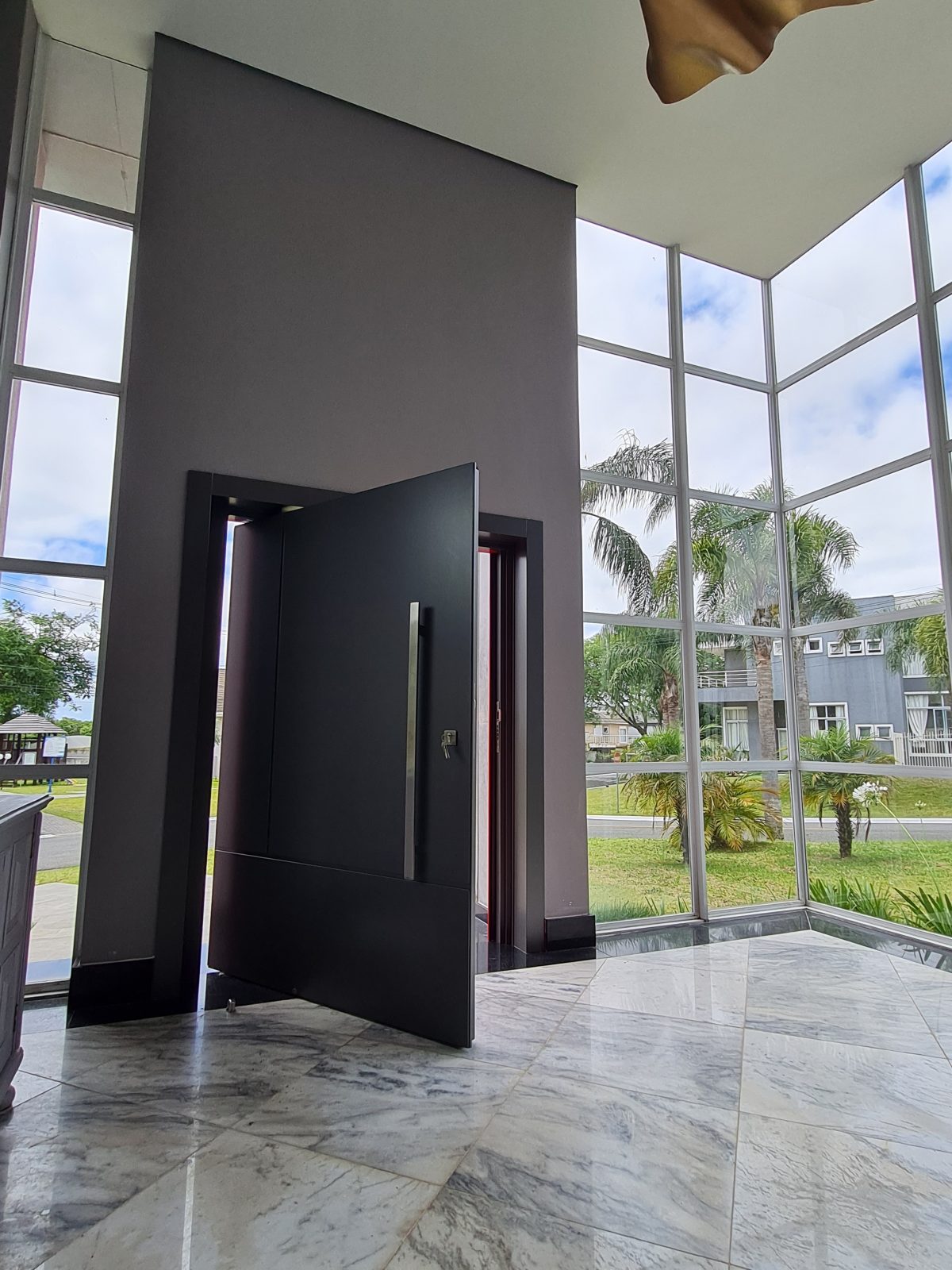 Porta pivotante em ACM com duas cores. Lado externo vermelho fosco e lado interno cinza. Painéis e bandeira fixos seguindo mesmo alinhamento da porta e dupla vedação. - Imagem 11