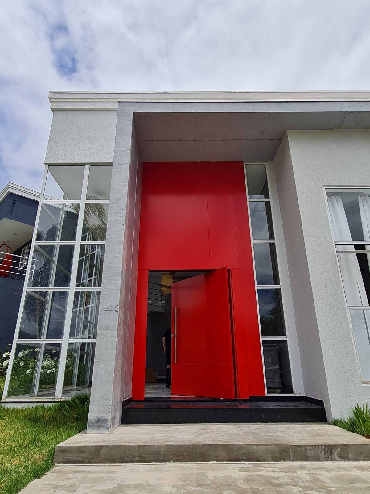 Porta pivotante em ACM com duas cores. Lado externo vermelho fosco e lado interno cinza. Painéis e bandeira fixos seguindo mesmo alinhamento da porta e dupla vedação. - Imagem 2