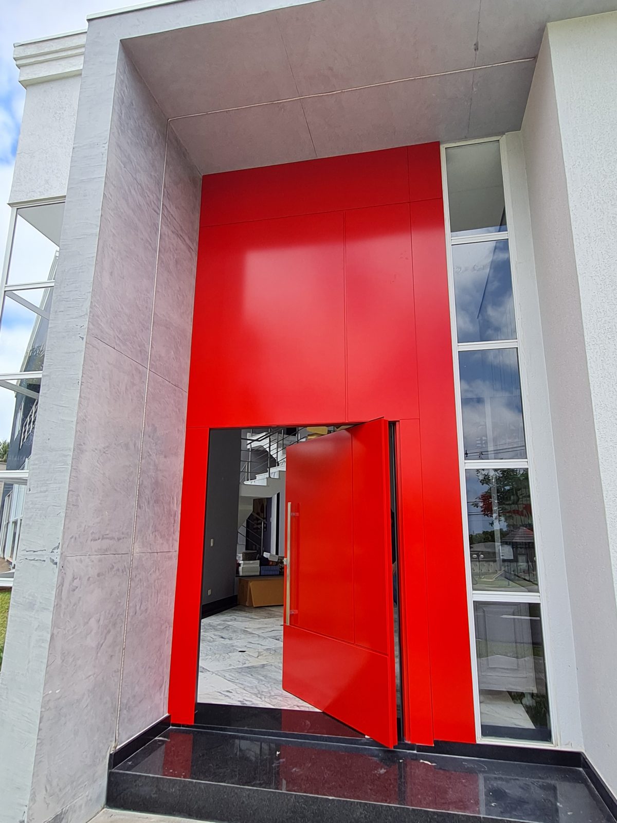 Porta pivotante em ACM com duas cores. Lado externo vermelho fosco e lado interno cinza. Painéis e bandeira fixos seguindo mesmo alinhamento da porta e dupla vedação. - Imagem 3