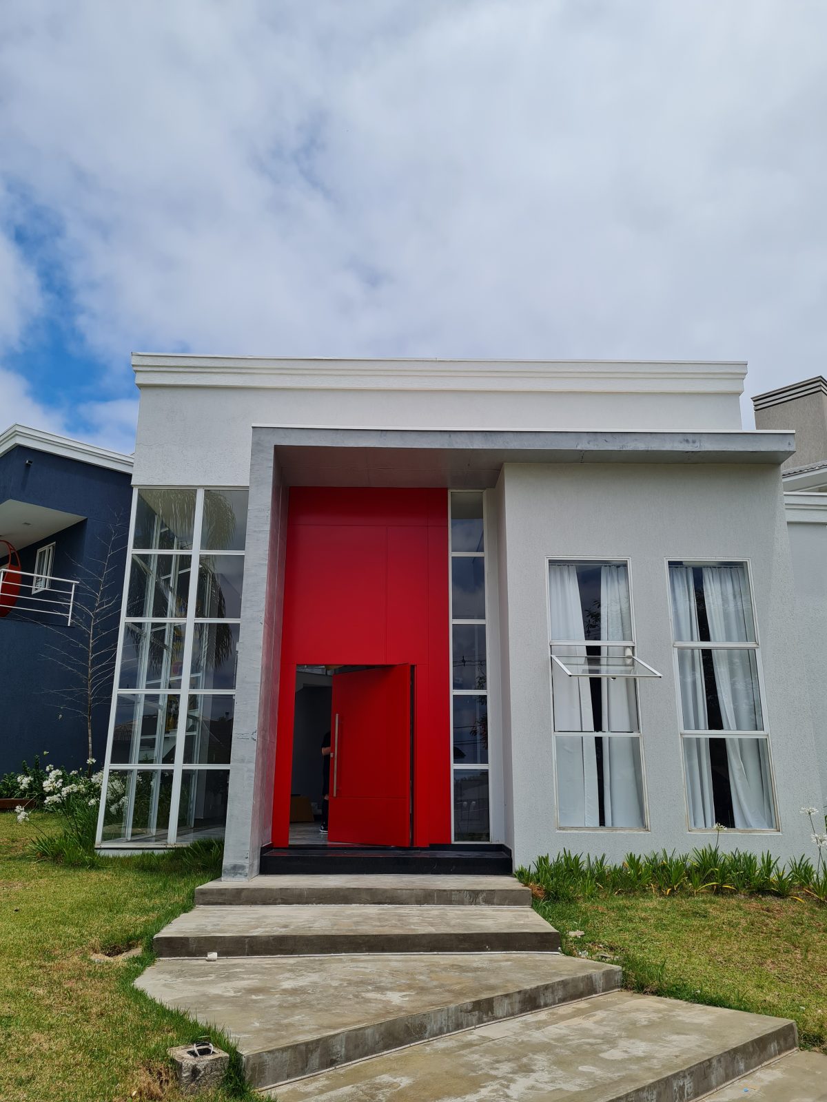 Porta pivotante em ACM com duas cores. Lado externo vermelho fosco e lado interno cinza. Painéis e bandeira fixos seguindo mesmo alinhamento da porta e dupla vedação. - Imagem 4