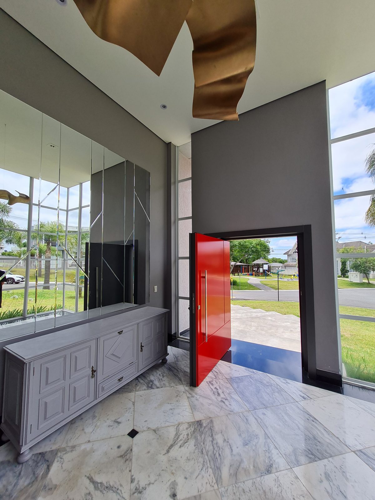 Porta pivotante em ACM com duas cores. Lado externo vermelho fosco e lado interno cinza. Painéis e bandeira fixos seguindo mesmo alinhamento da porta e dupla vedação. - Imagem 5