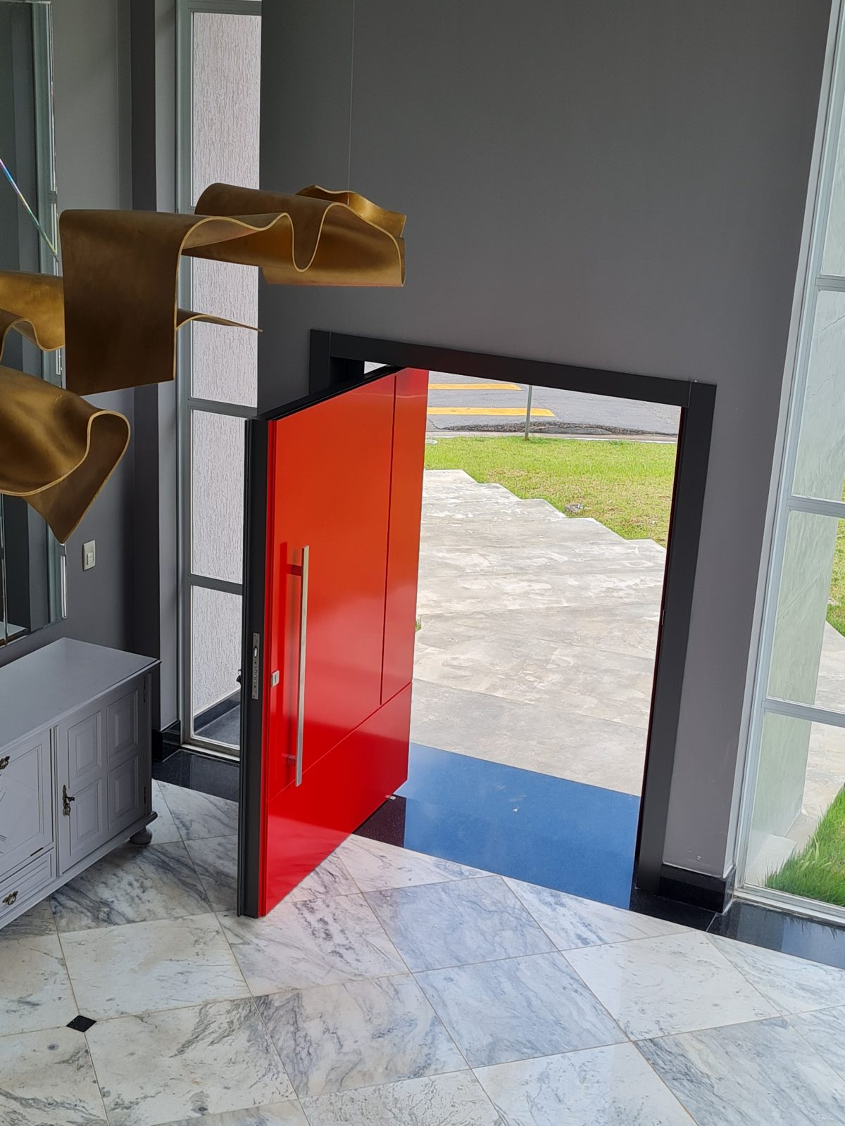 Porta pivotante em ACM com duas cores. Lado externo vermelho fosco e lado interno cinza. Painéis e bandeira fixos seguindo mesmo alinhamento da porta e dupla vedação. - Imagem 6
