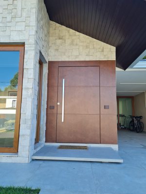 Porta em ACM aço corten, modelo com frisos, painéis laterais fixos no mesmo alinhamento da porta, dupla vedação porta e batente