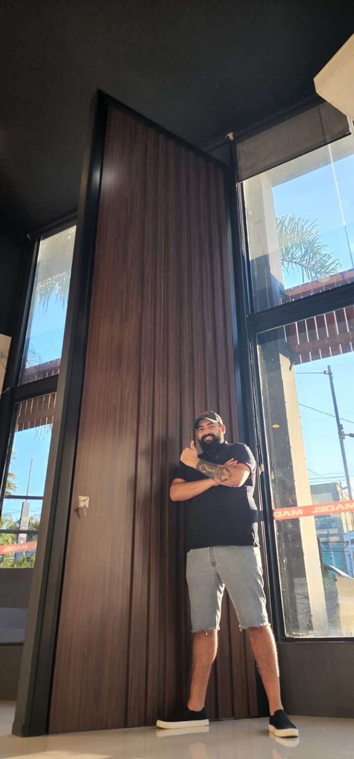 Porta pivotante em ACM ripado na vertical cor Sucupira e dupla vedação ...