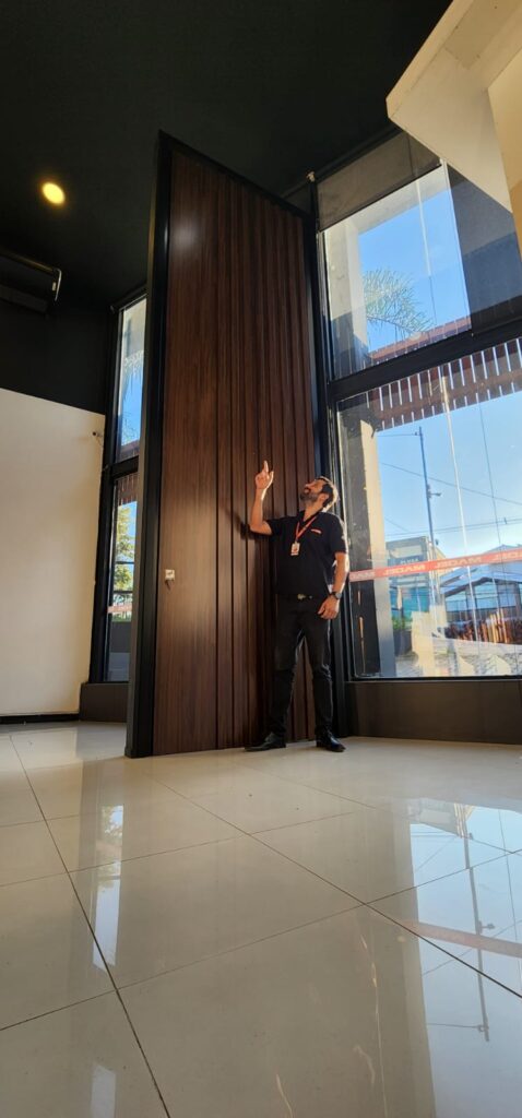 Porta pivotante em ACM ripado na vertical cor Sucupira e dupla vedação ...