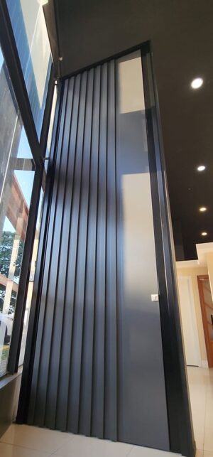 Porta pivotante em ACM ripado na vertical cor Dark Grey e dupla vedação