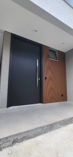 Porta pivotante em ACM preto fosco, painel fixo ripado madeirado, dupla vedação porta e batente