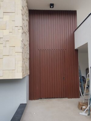 Porta pivotante em ACM modelo ripado vertical puxador cava no prórprio ripado e dupla vedação porta e batente