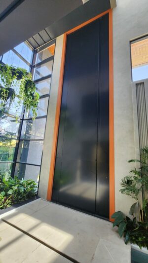 Porta pivotante em ACM preto fosco com puxador cava, batente e guarnições em ACM Wood Cerejeira