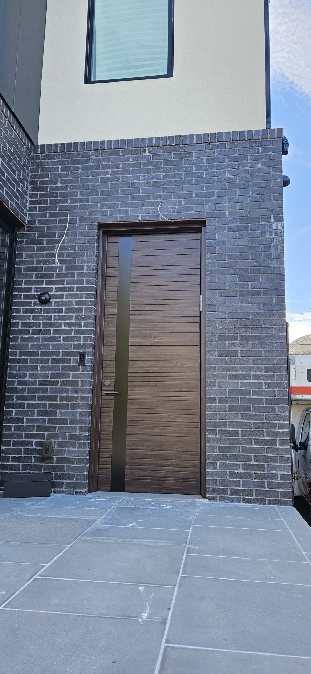 Porta pivotante em ACM Wood Sucupira com frisos horizontais e detalhe em ACM preto - Imagem 1