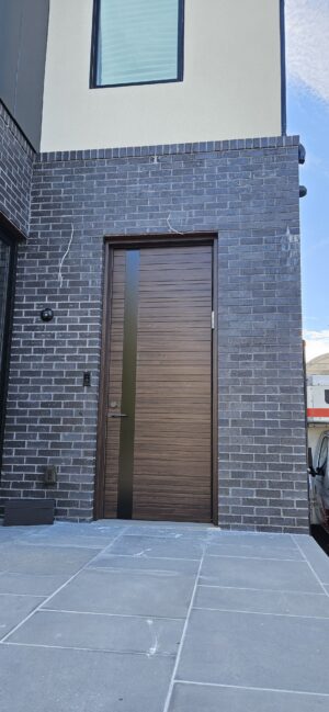 Porta pivotante em ACM Wood Sucupira com frisos horizontais e detalhe em ACM preto