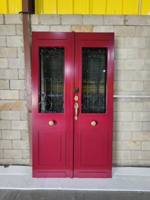 Porta em ACM com sistema de abertura dupla em estilo colonial, equipada com grade em ferro, aldrava decorativa, fechaduras blim blim e digital