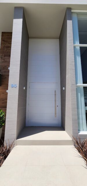 Porta pivotante em ACM com frisos horizontais e bandeira superior fixa. Modelo moderno, resistente e elegante, ideal para valorizar a fachada