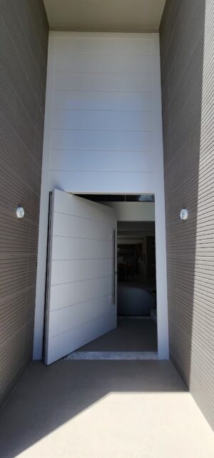 Porta pivotante em ACM com frisos horizontais e bandeira superior fixa. Modelo moderno, resistente e elegante, ideal para valorizar a fachada - Imagem 2