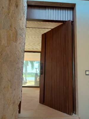 Porta pivotante em ACM com puxador cava, modelo ripado vertical e bandeira superior fixa, destacando design moderno e elegante - Imagem 2