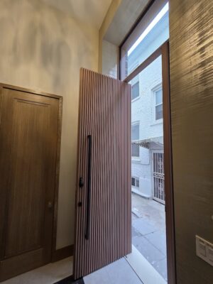 Porta pivotante em ACM modelo ripado, com portal e bandeira em vidro, destacando leveza e sofisticação no projeto - Imagem 4