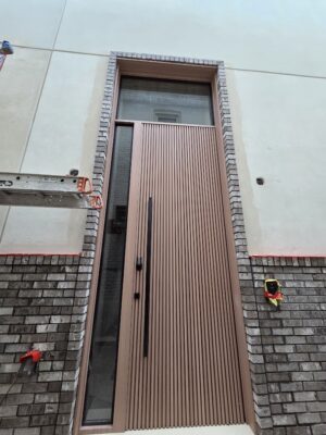 Porta pivotante em ACM modelo ripado, com portal e bandeira em vidro, destacando leveza e sofisticação no projeto